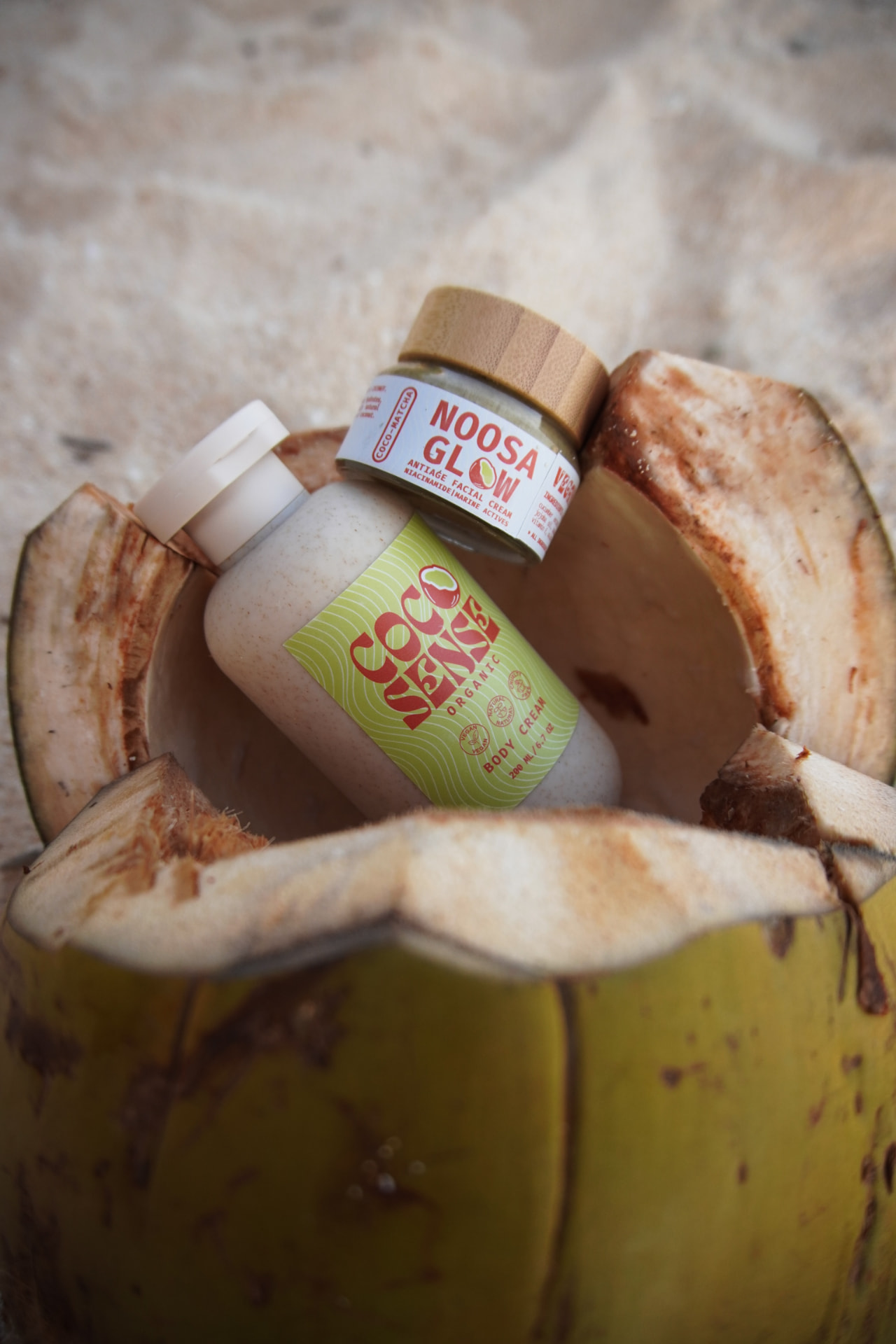 Coco Sense organic body cream and Noosa Glow matcha facial cream set inside a cracked coconut