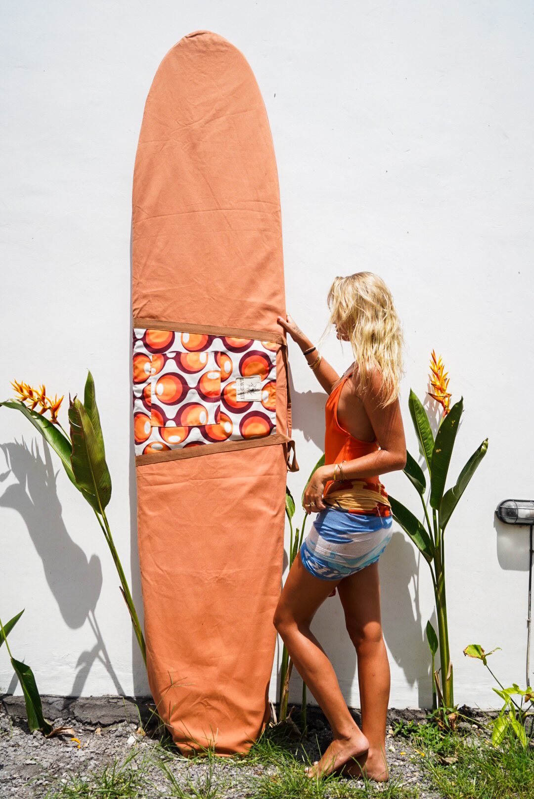 Orange Barefeet Surf board bag displayed beside tropical plants